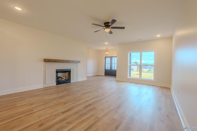 unfurnished living room with ceiling fan with notable chandelier and light hardwood / wood-style flooring