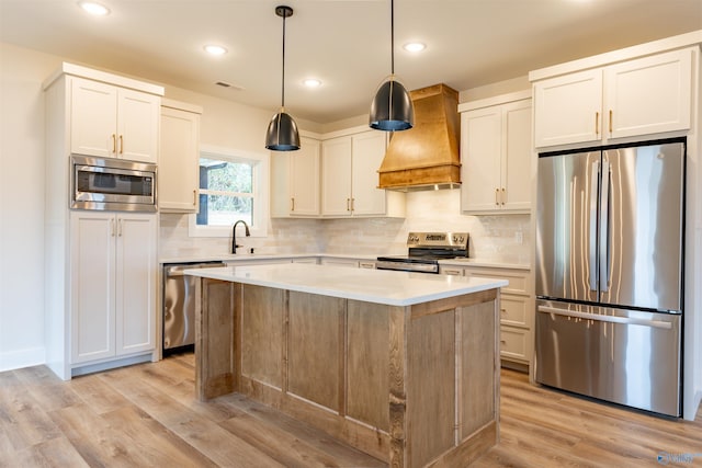 kitchen featuring light wood-type flooring, custom range hood, stainless steel appliances, a center island, and white cabinetry