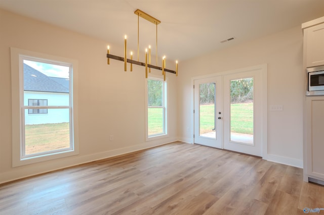 unfurnished dining area featuring french doors, a notable chandelier, and light wood-type flooring