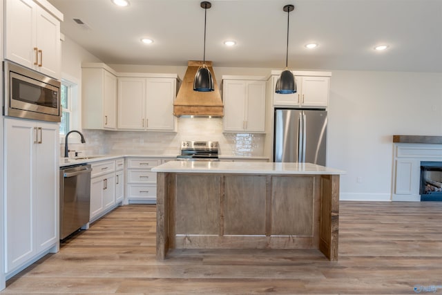 kitchen with hanging light fixtures, sink, custom range hood, appliances with stainless steel finishes, and white cabinetry