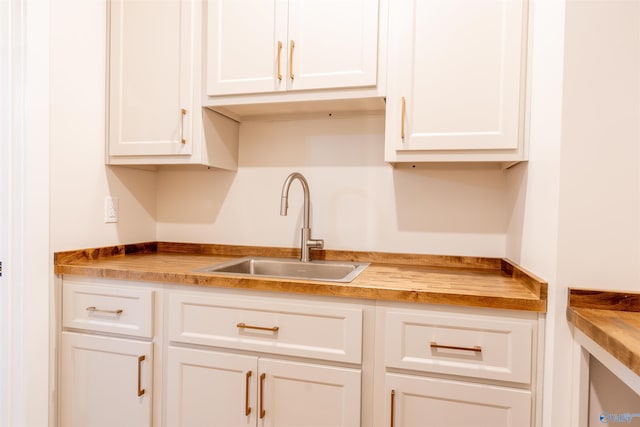 kitchen with wood counters, white cabinetry, and sink