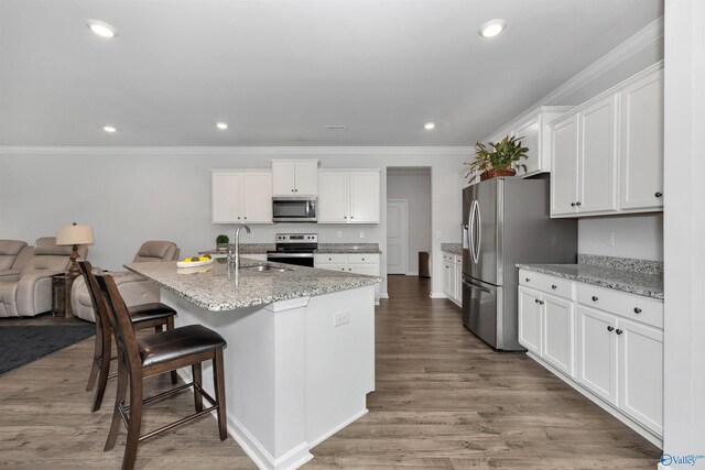 kitchen with light stone countertops, a center island with sink, stainless steel appliances, sink, and light wood-type flooring