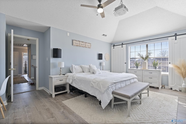 bedroom featuring vaulted ceiling, ceiling fan, a barn door, a textured ceiling, and light wood-type flooring