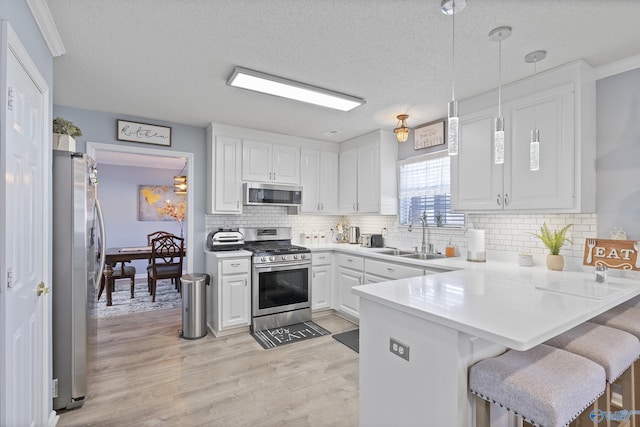 kitchen with sink, appliances with stainless steel finishes, kitchen peninsula, pendant lighting, and white cabinets