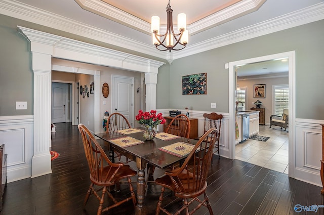 dining space featuring sink, a tray ceiling, hardwood / wood-style floors, a chandelier, and crown molding