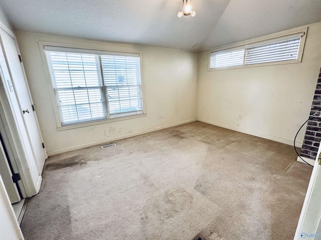 carpeted empty room with a textured ceiling and vaulted ceiling