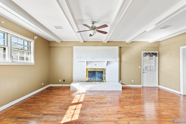 unfurnished living room featuring beam ceiling, ceiling fan, a brick fireplace, and light hardwood / wood-style flooring