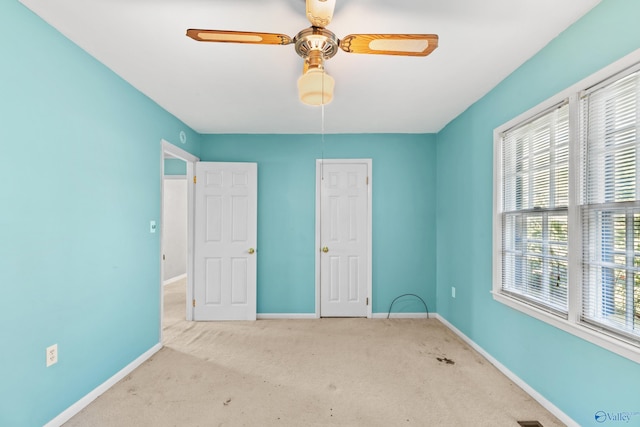 unfurnished bedroom featuring multiple windows, light colored carpet, and ceiling fan