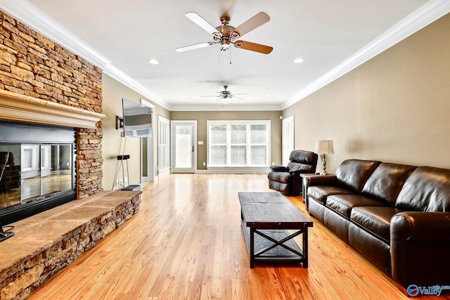 living room with light hardwood / wood-style floors, a stone fireplace, ornamental molding, and ceiling fan