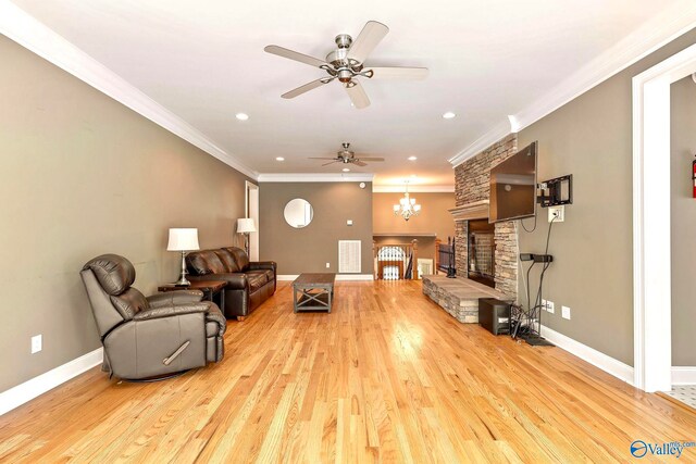 living room with ornamental molding, a stone fireplace, ceiling fan with notable chandelier, and light wood-type flooring