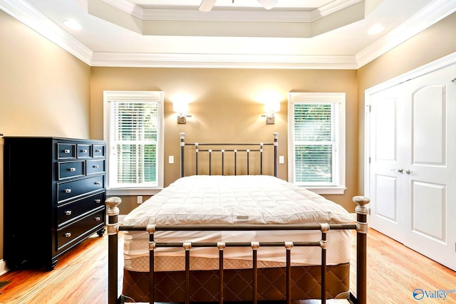 bedroom featuring ceiling fan, a tray ceiling, light hardwood / wood-style flooring, crown molding, and a closet