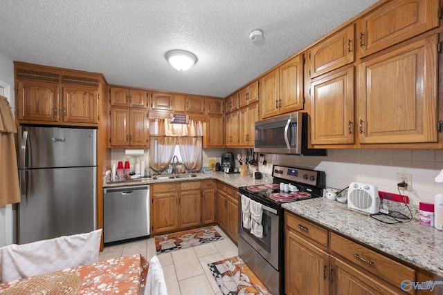 kitchen featuring sink, light stone counters, light tile patterned floors, appliances with stainless steel finishes, and backsplash