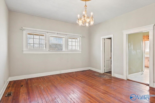 empty room with a healthy amount of sunlight, hardwood / wood-style floors, and an inviting chandelier