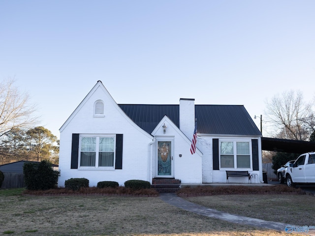 view of front of home featuring brick siding, a chimney, entry steps, metal roof, and a carport