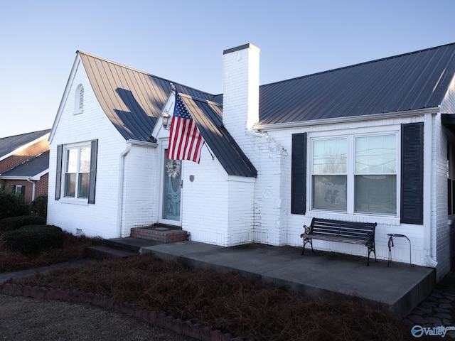 view of front of home featuring entry steps, brick siding, metal roof, and a chimney