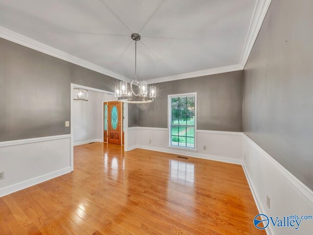 unfurnished dining area featuring ornamental molding, light wood-type flooring, baseboards, visible vents, and a notable chandelier