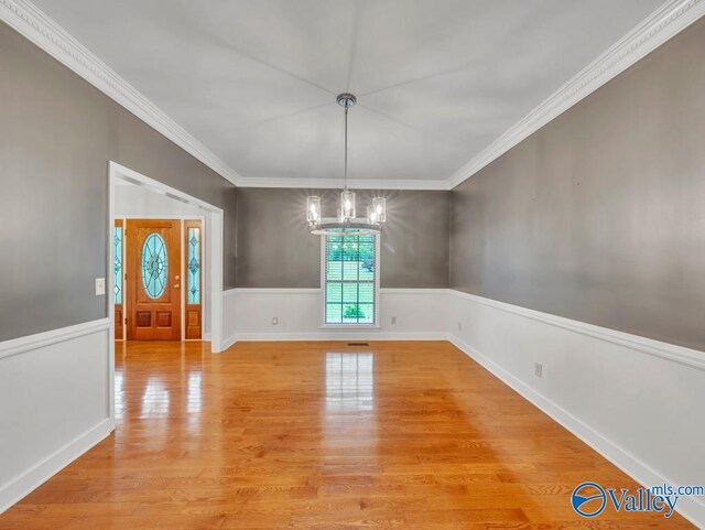 unfurnished dining area with crown molding, a chandelier, baseboards, light wood-type flooring, and wainscoting
