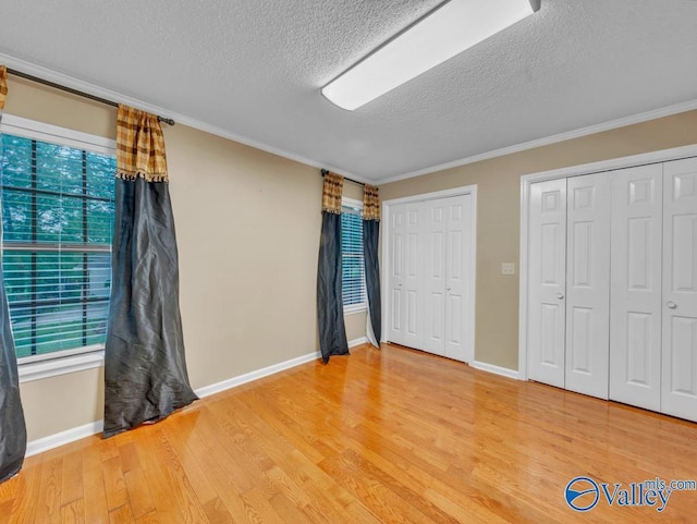 unfurnished bedroom featuring light wood-style flooring, multiple closets, ornamental molding, baseboards, and a textured ceiling