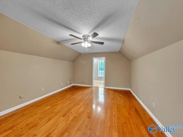 additional living space with vaulted ceiling, baseboards, light wood-type flooring, a ceiling fan, and a textured ceiling