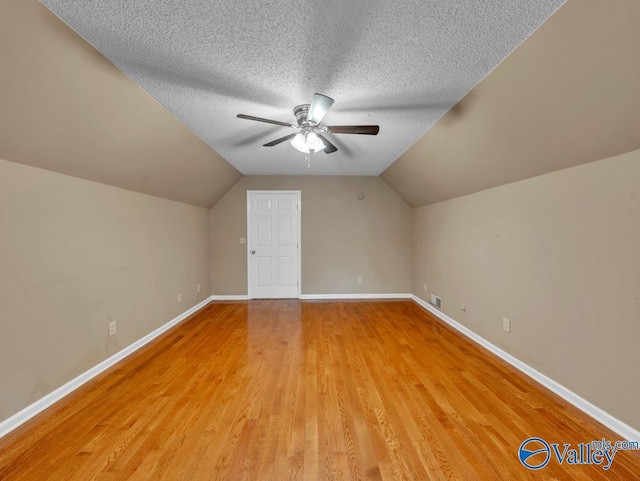 bonus room featuring light wood-style floors, ceiling fan, baseboards, a textured ceiling, and lofted ceiling