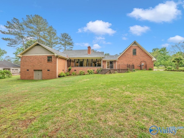back of house with a chimney, brick siding, a yard, and a sunroom