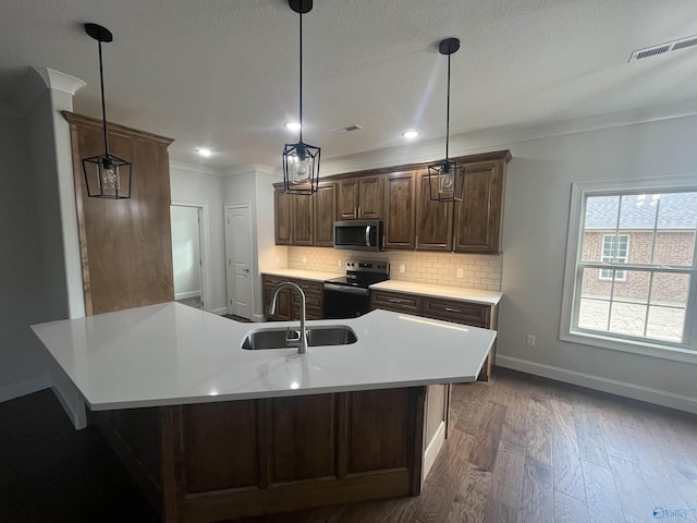 kitchen with sink, hanging light fixtures, appliances with stainless steel finishes, and an island with sink