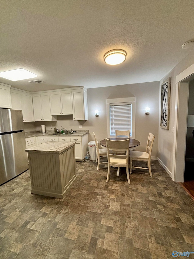 kitchen featuring sink, stainless steel fridge, white cabinets, and a textured ceiling