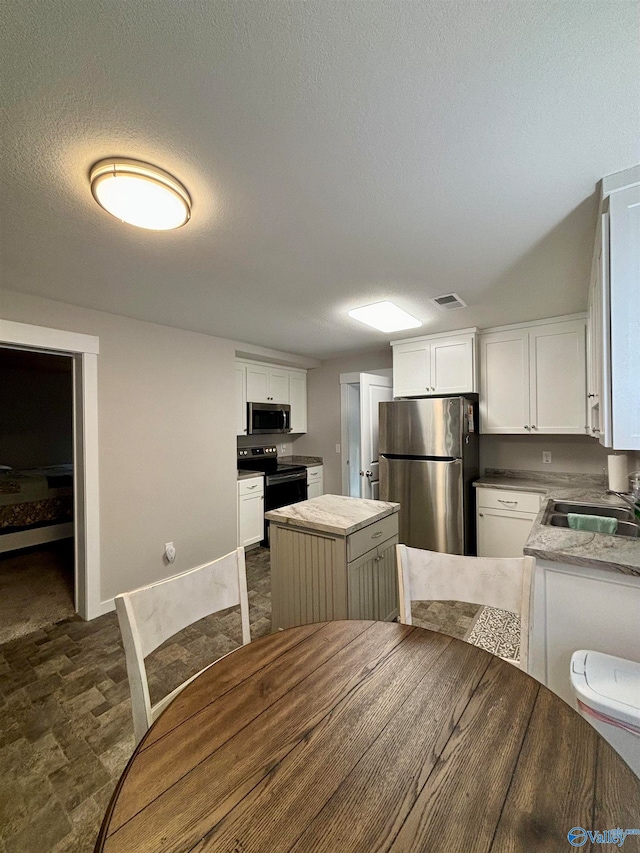 kitchen with stainless steel appliances, sink, a center island, white cabinetry, and a textured ceiling