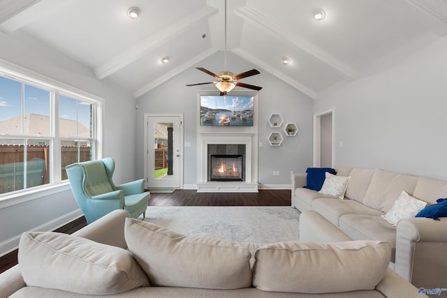 living area featuring baseboards, a tiled fireplace, vaulted ceiling with beams, and dark wood-type flooring