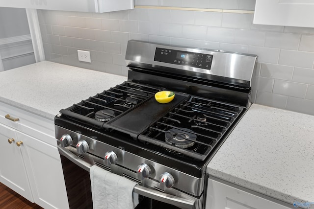 interior details with white cabinetry, decorative backsplash, and stainless steel gas stove