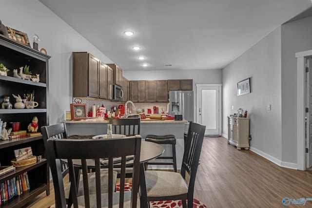 kitchen featuring dark brown cabinets, stainless steel appliances, tasteful backsplash, wood-type flooring, and a kitchen bar