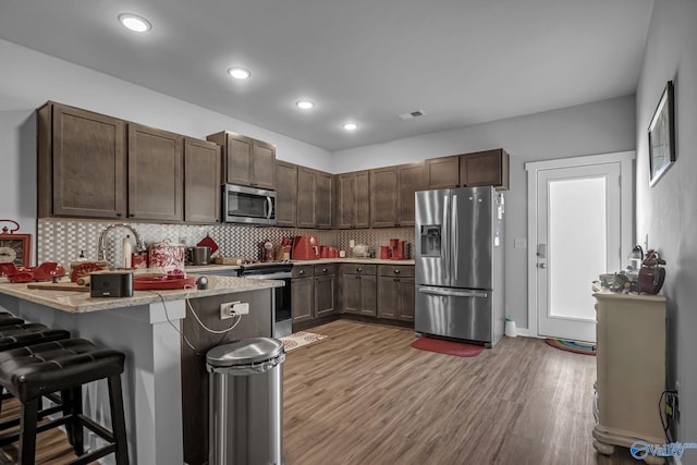 kitchen with appliances with stainless steel finishes, a breakfast bar area, dark brown cabinetry, and kitchen peninsula