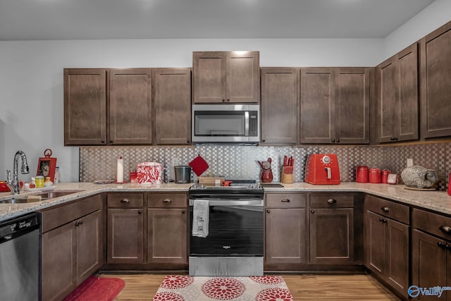 kitchen with sink, light wood-type flooring, stainless steel appliances, and light stone countertops