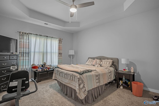 carpeted bedroom with a tray ceiling and ceiling fan