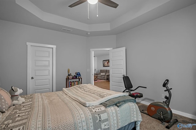 carpeted bedroom with a tray ceiling and ceiling fan