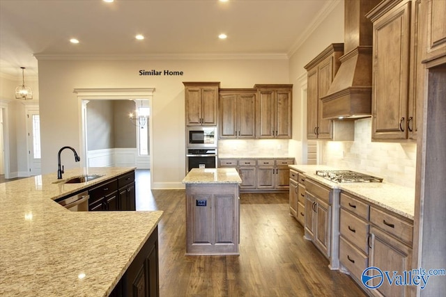 kitchen featuring wall chimney range hood, light stone counters, a sink, appliances with stainless steel finishes, and a kitchen island