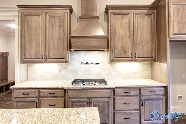 kitchen featuring stainless steel gas stovetop, decorative backsplash, ornamental molding, and custom range hood