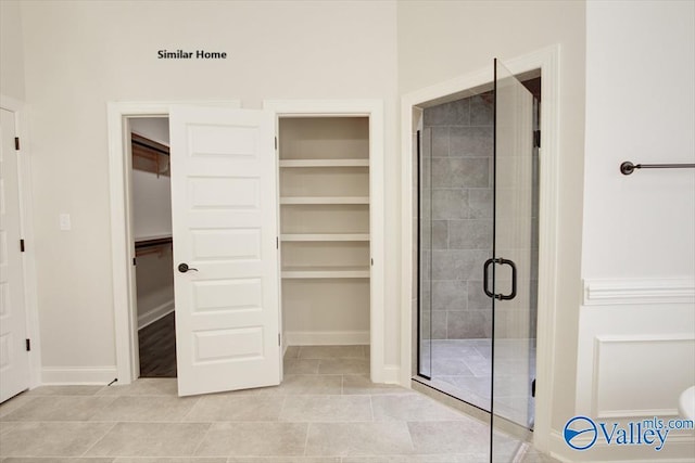 bathroom with a spacious closet, baseboards, tile patterned floors, and a stall shower