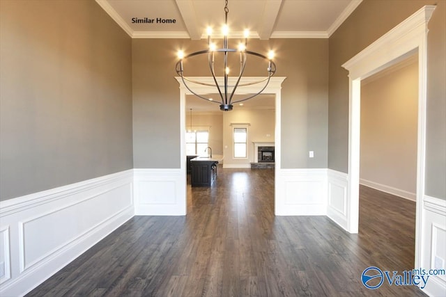 unfurnished dining area featuring wainscoting, dark wood-style flooring, ornamental molding, and a chandelier