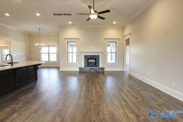 unfurnished living room featuring dark wood-style floors, a sink, baseboards, ceiling fan with notable chandelier, and a fireplace