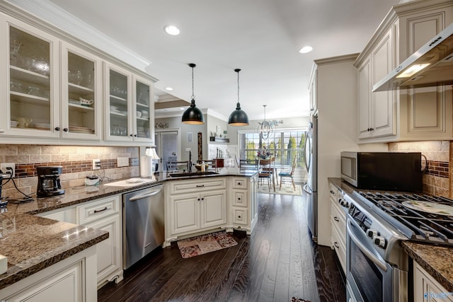 kitchen with stainless steel appliances, sink, wall chimney exhaust hood, dark stone counters, and pendant lighting