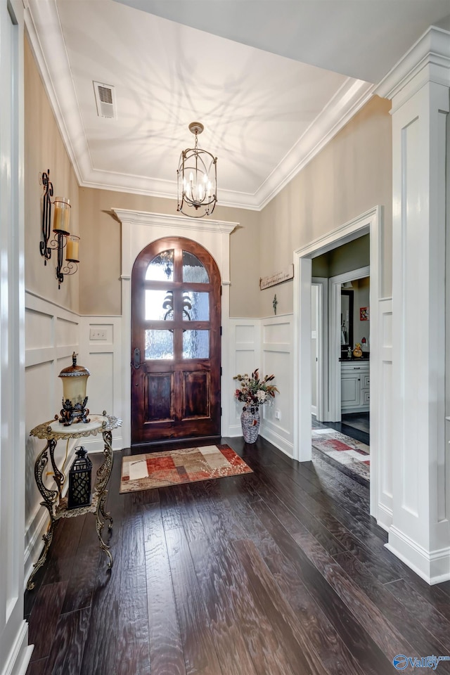 foyer with dark wood-type flooring, crown molding, and a chandelier