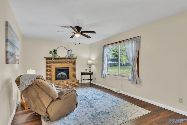 living room featuring ceiling fan, a fireplace, and dark wood-type flooring