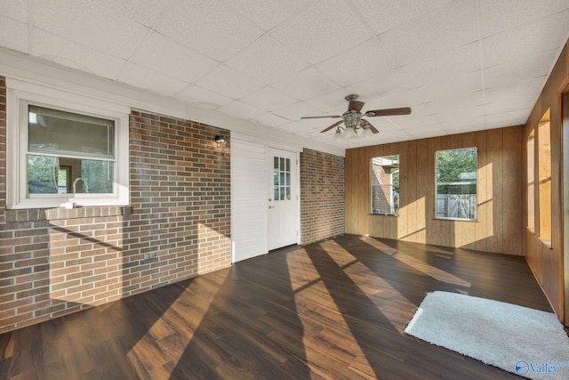 empty room featuring a paneled ceiling, wood walls, brick wall, and dark hardwood / wood-style floors