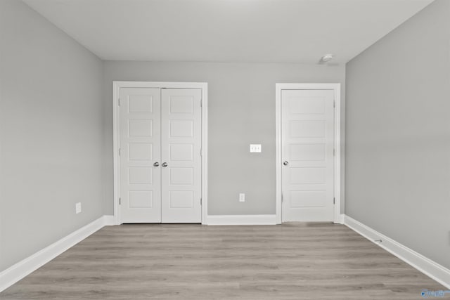 unfurnished bedroom featuring light wood-style flooring, baseboards, and a closet