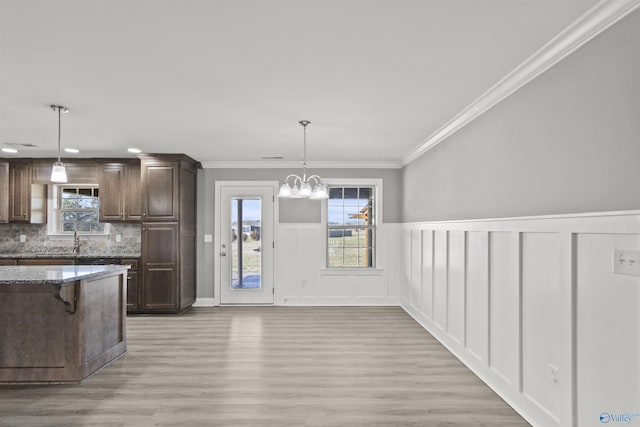 kitchen featuring a chandelier, dark stone counters, ornamental molding, decorative backsplash, and light wood-style floors