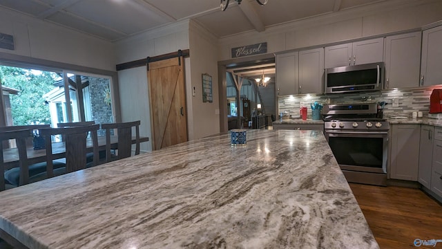 kitchen featuring backsplash, stainless steel appliances, a barn door, and gray cabinetry