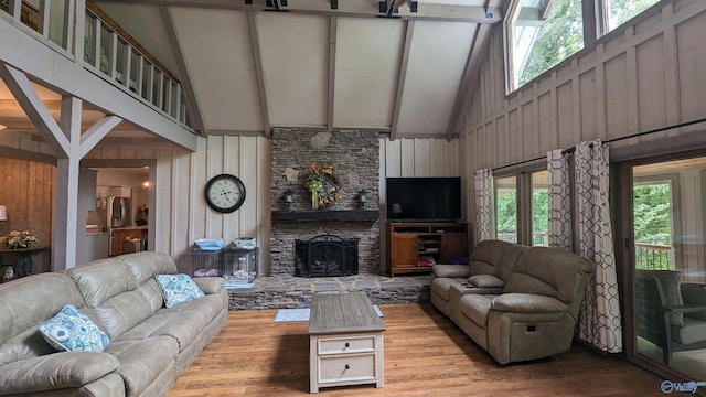 living area featuring wooden walls, beamed ceiling, light wood-style floors, a fireplace, and high vaulted ceiling