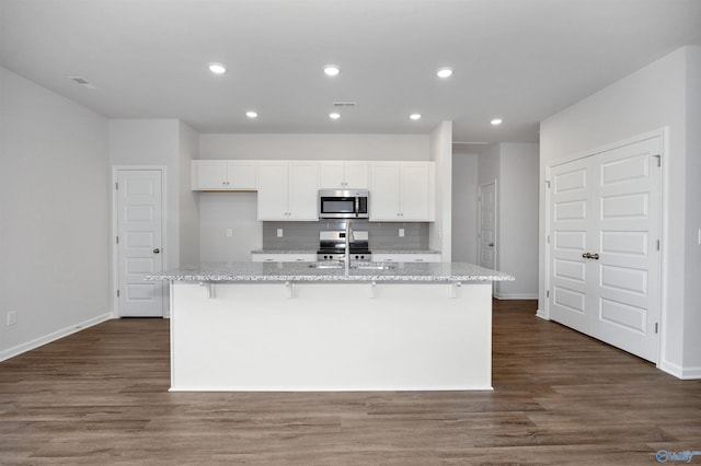 kitchen with a kitchen island with sink, light stone counters, a breakfast bar area, and stainless steel appliances