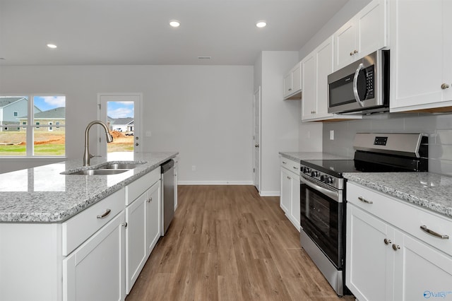 kitchen with sink, white cabinetry, stainless steel appliances, light hardwood / wood-style floors, and an island with sink